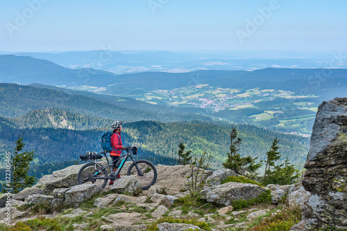active senior woman on a bike packing tour with her electric mountain bike in the rocky  the summit of Great Arber in the Bavarian Forest, Bavaria, Germany