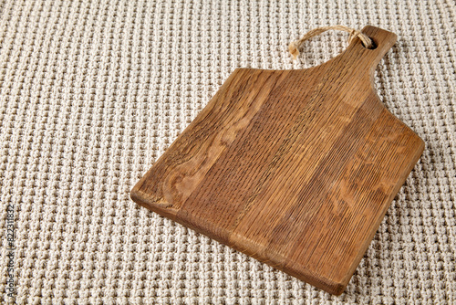 A blank brown wooden cutting board on a table draped with a beige knitted plaid blanket