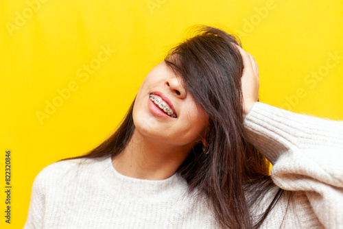 young asian girl with braces smiling with closed eyes on yellow isolated background, korean girl showing face and smile