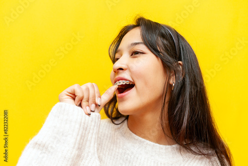 I bet you. young asian woman with braces showing promise gesture and touching tooth with finger on yellow isolated background, korean girl showing dental smile and dental care