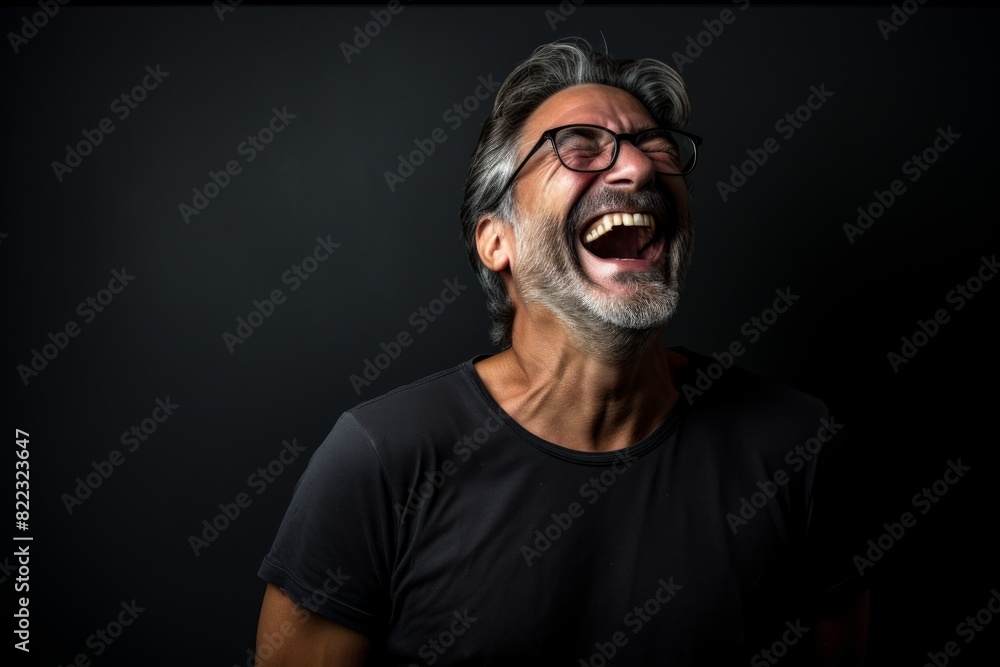 Portrait of a glad man in his 50s laughing in front of bare monochromatic room