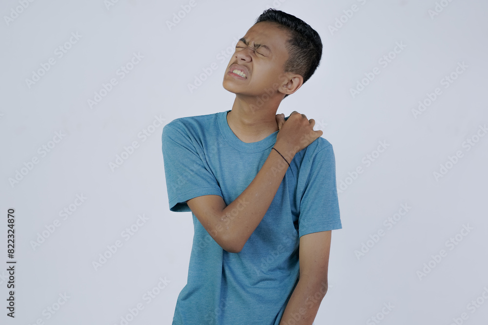 young Asian man in blue shirt holding his shoulder in pain, joint disease, isolated in gray background. young Asian man in blue shirt holding his shoulder in pain, joint disease, isolated in gray background.