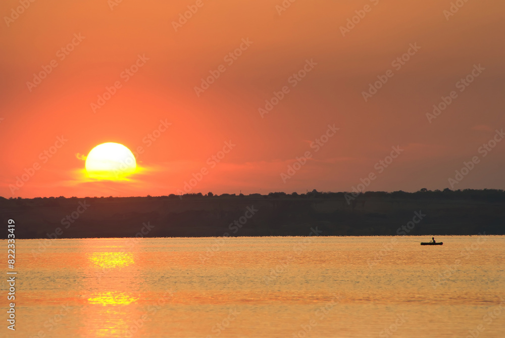South Bug estuary in area of ancient Greek city state Olvia. Yellow sunset after hot day and dense water haze over water due to high humidity. Solar halo. Fisherman in boat in middle of estuary South Bug estuary in area of ancient Greek city state Olvia. Yellow sunset after hot day and dense water haze over water due to high humidity. Solar halo. Fisherman in boat in middle of estuary