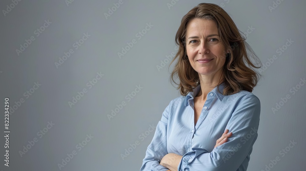 confident professional businesswoman in blue shirt with arms crossed smiling at camera gray background confident professional businesswoman in blue shirt with arms crossed smiling at camera gray background