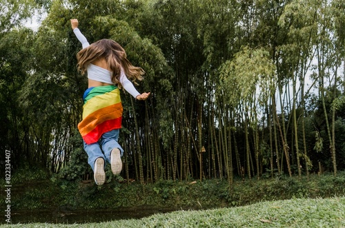 joven mujer al aire libre y la bandera del orgullo gay en su cintura saltando de felicidad  photo