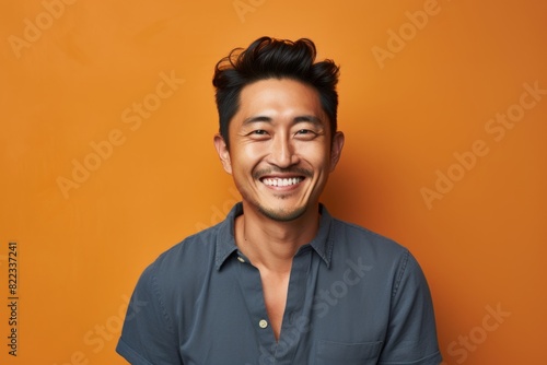 Portrait of a joyful asian man in his 30s smiling at the camera in front of plain cyclorama studio wall
