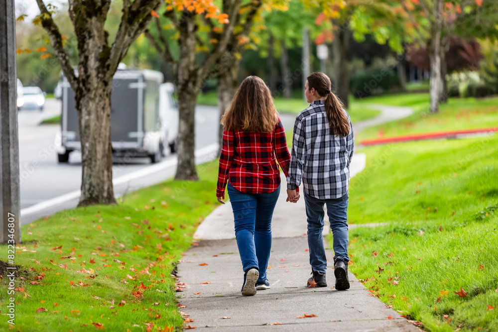 A teenage boy and girl walking down a sidewalk holding hands; Bothell, Washington, United States of America A teenage boy and girl walking down a sidewalk holding hands; Bothell, Washington, United States of America