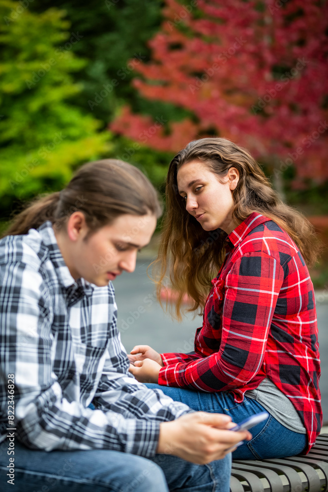 A young couple sitting on a bench using their smart phones; Bothell, Washington, United States of America A young couple sitting on a bench using their smart phones; Bothell, Washington, United States of America