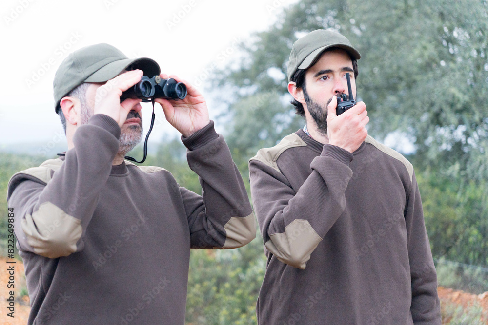 Two male rangers working in nature with walkie-talkies and binoculars Two male rangers working in nature with walkie-talkies and binoculars