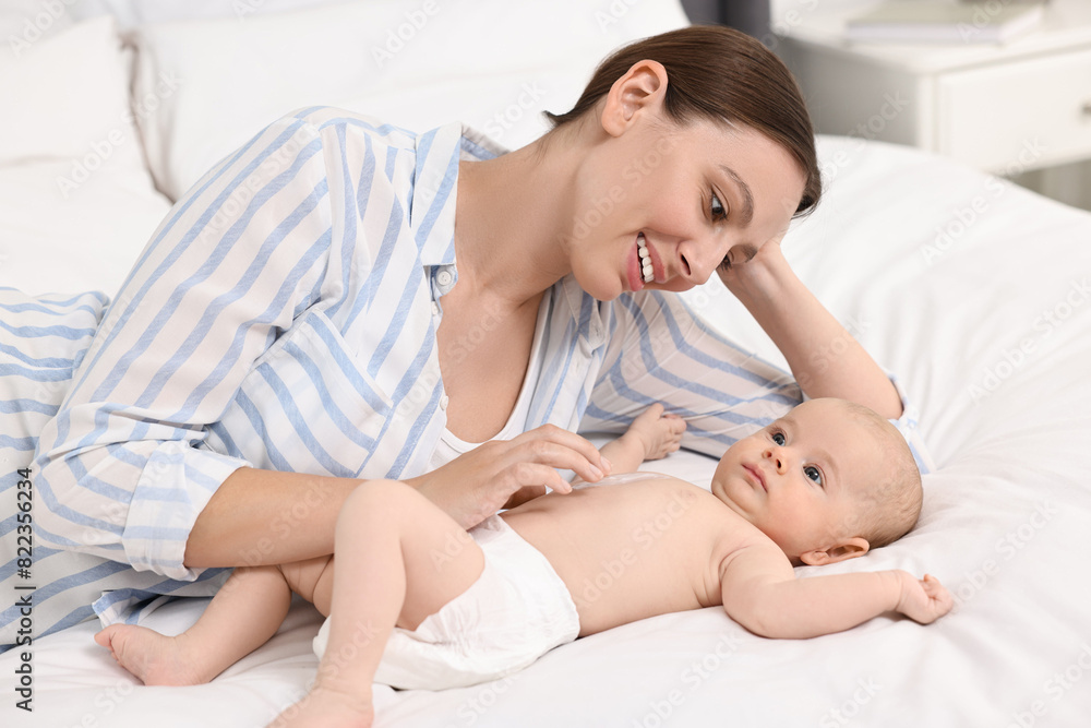 Happy young woman applying body cream onto baby`s skin on bed