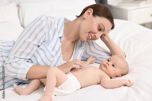 Happy young woman applying body cream onto baby s skin on bed