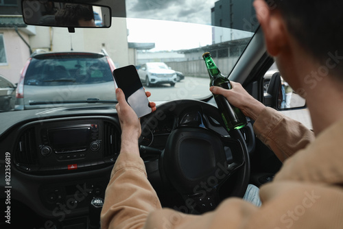 Man with bottle of beer and smartphone in car, closeup. Don't drink and drive concept photo
