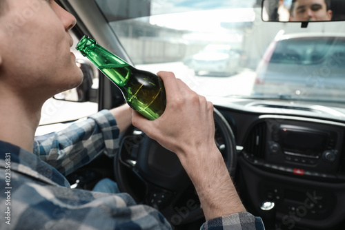 Man with bottle of beer driving car, closeup. Don't drink and drive concept photo