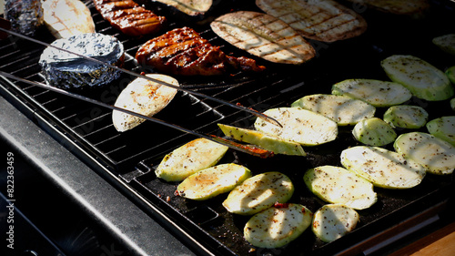 Close-up of spiced ​​zucchini, eggplant slices, cheese in foil, marinated chicken breast and grill tongs on a gas grill taken in evening light. Summer evening dinner. Home made food concept.