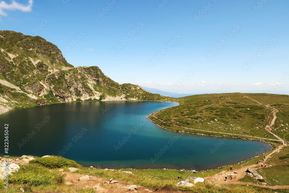 The deep blue Kidney, Babreka Lake, one of the Seven Rila Lakes, situated on a plateau in the Rila National Park, a few people are on the hiking trail right next to it, close to Sofia, Bulgaria