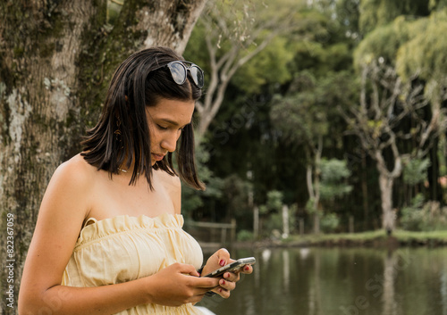 joven mujer hispanoamericana escribe mensaje de texto al aire libre en el parque  photo