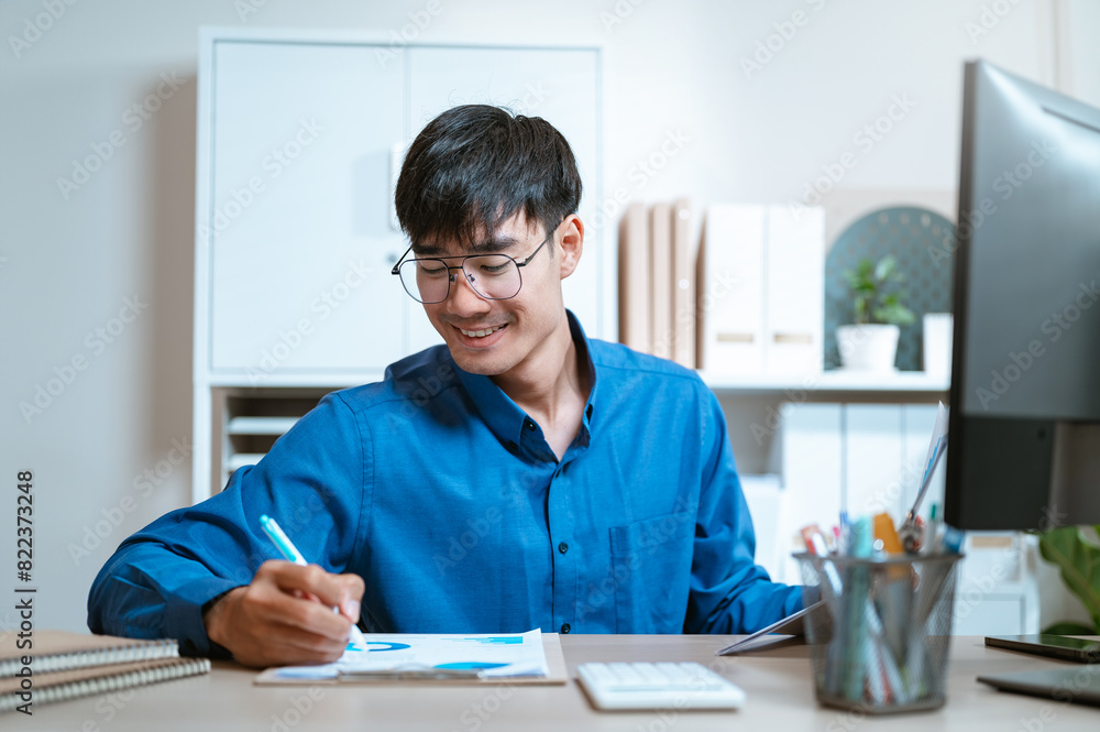 document, thinking, working, writing, executive, expertise, ideas, planning, job, management. A man is sitting with a blue shirt on and writing with a blue pen. He is smiling and enjoying himself. document, thinking, working, writing, executive, expertise, ideas, planning, job, management. A man is sitting with a blue shirt on and writing with a blue pen. He is smiling and enjoying himself.