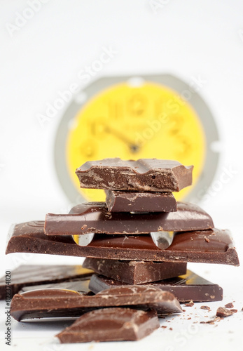 stack of broken chocolate bars , on background alarm clock