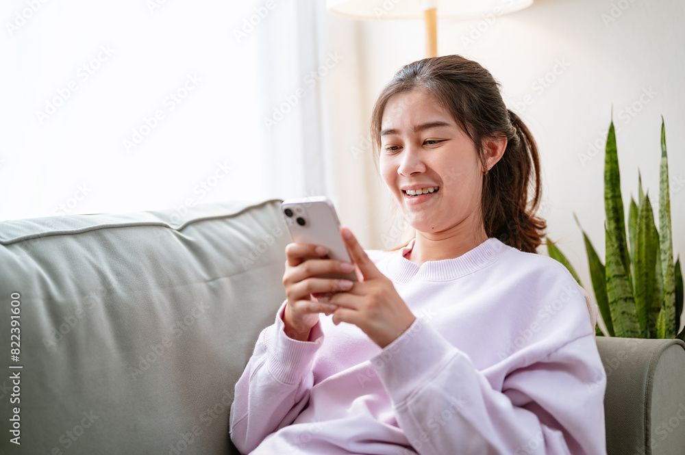 sofa, couch, chat, sitting, sms, smartphone, living, message, communication, reading. A woman is sitting on a couch and looking at her cell phone. She is smiling and she is enjoying herself. sofa, couch, chat, sitting, sms, smartphone, living, message, communication, reading. A woman is sitting on a couch and looking at her cell phone. She is smiling and she is enjoying herself.