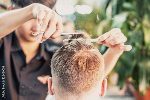 Neat young Vietnamese hairdresser makes haircut to male. Back view. Professional skills