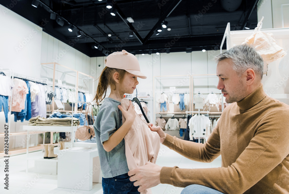 Father Helping Daughter Try on Clothes in Modern Clothing Store During Afternoon Father Helping Daughter Try on Clothes in Modern Clothing Store During Afternoon