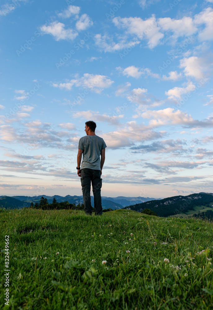 Person Standing on Green Hilltop Admiring Mountain Views and Cloudy Sky at Sunset Person Standing on Green Hilltop Admiring Mountain Views and Cloudy Sky at Sunset