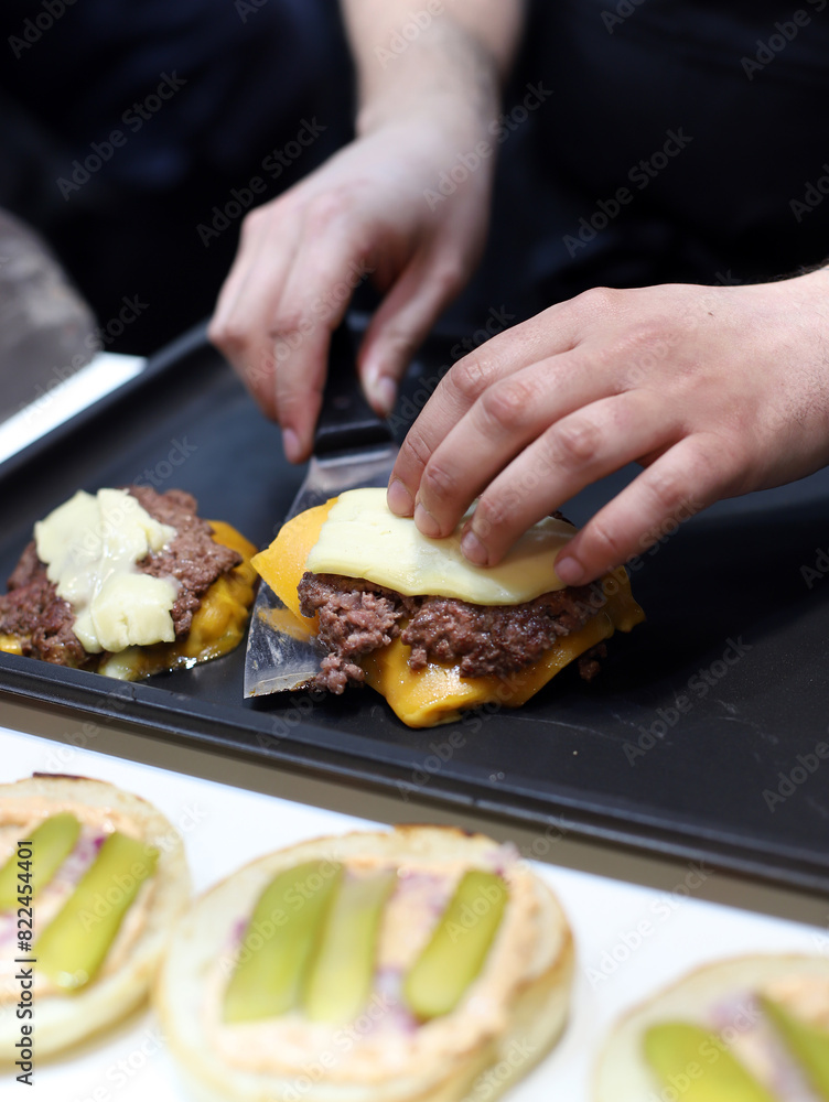 chef sirviendo una hamburguesa de carne y queso fundido recién frita a la plancha con sus manos y una paleta de cocina