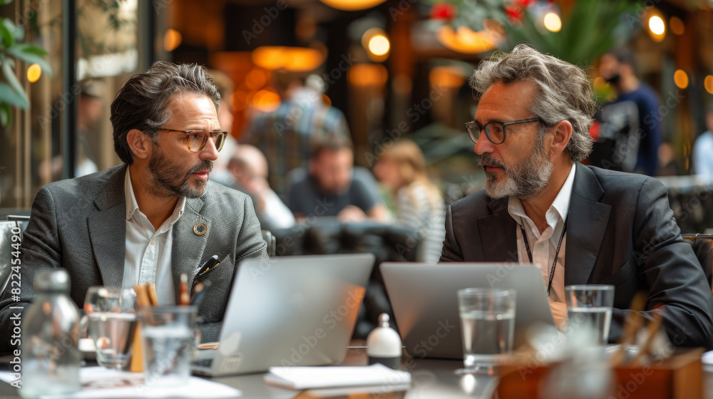 business collaboration, two businessmen discussing terms of their collaboration in a stylish cafe, laptops on the table, half-empty glasses of water, surrounded by a busy atmosphere business collaboration, two businessmen discussing terms of their collaboration in a stylish cafe, laptops on the table, half-empty glasses of water, surrounded by a busy atmosphere