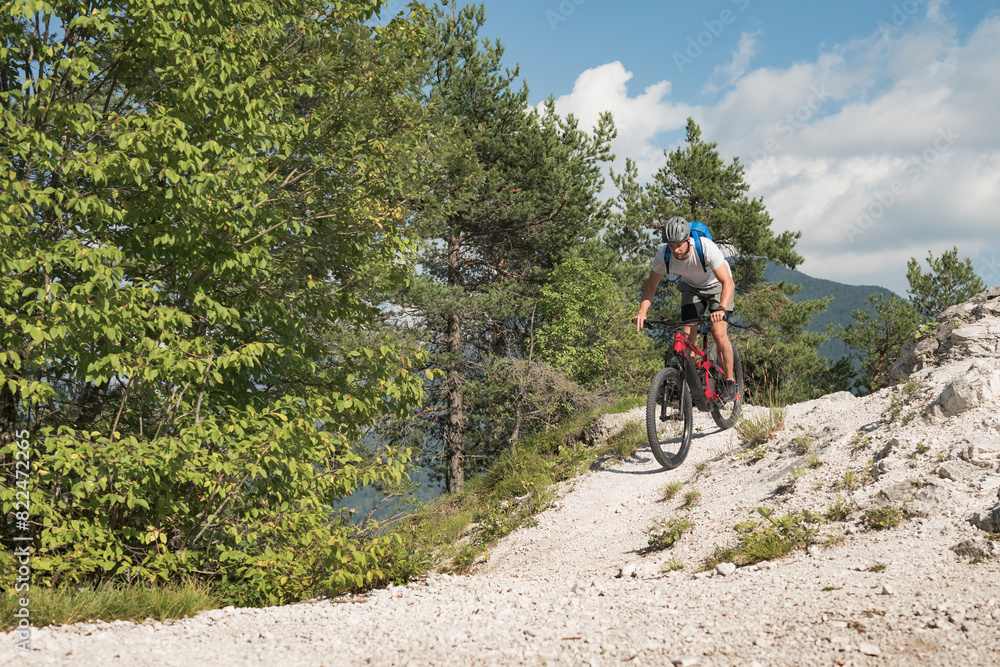 Mountain bike rider riding an electric bike along a white gravel trail on a sunny summer day. Outdoor sports activity concept.