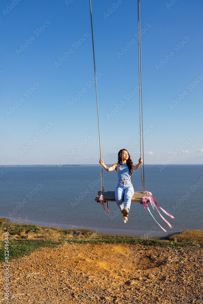 Attractive Asian girl in casual clothes swinging on an outdoor swing