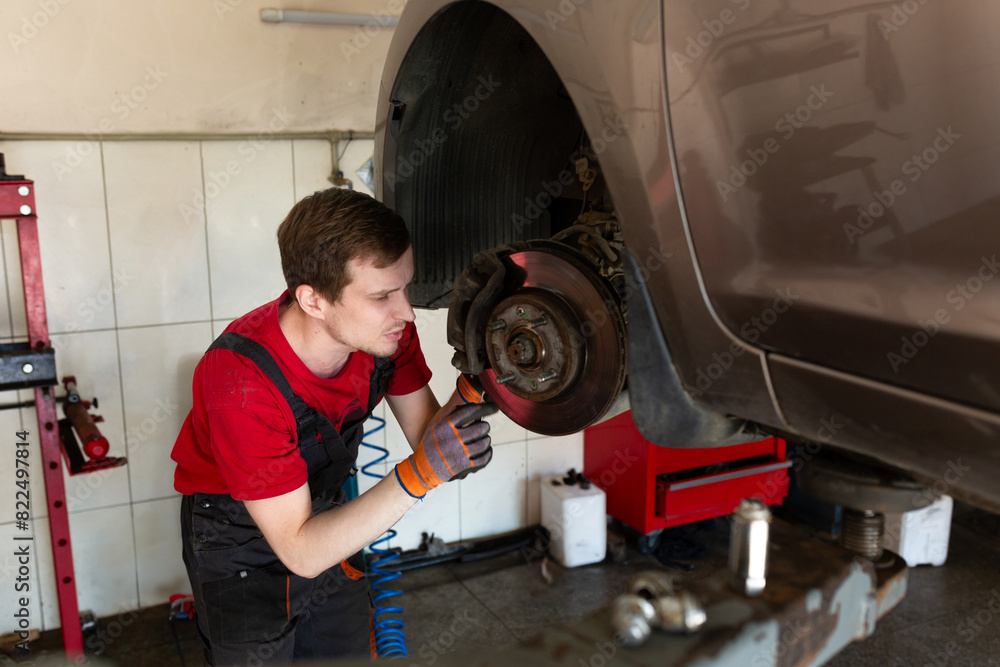 a mechanic stands by a car in a car service center. master repairs car brake discs and pads a mechanic stands by a car in a car service center. master repairs car brake discs and pads