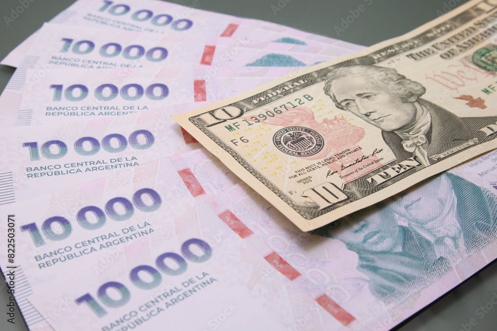 Stack of several thousand Argentine pesos banknotes and one hundred dollar on dark background. Relationship between pesos and dollars, Concept Dolar Blue Stack of several thousand Argentine pesos banknotes and one hundred dollar on dark background. Relationship between pesos and dollars, Concept Dolar Blue