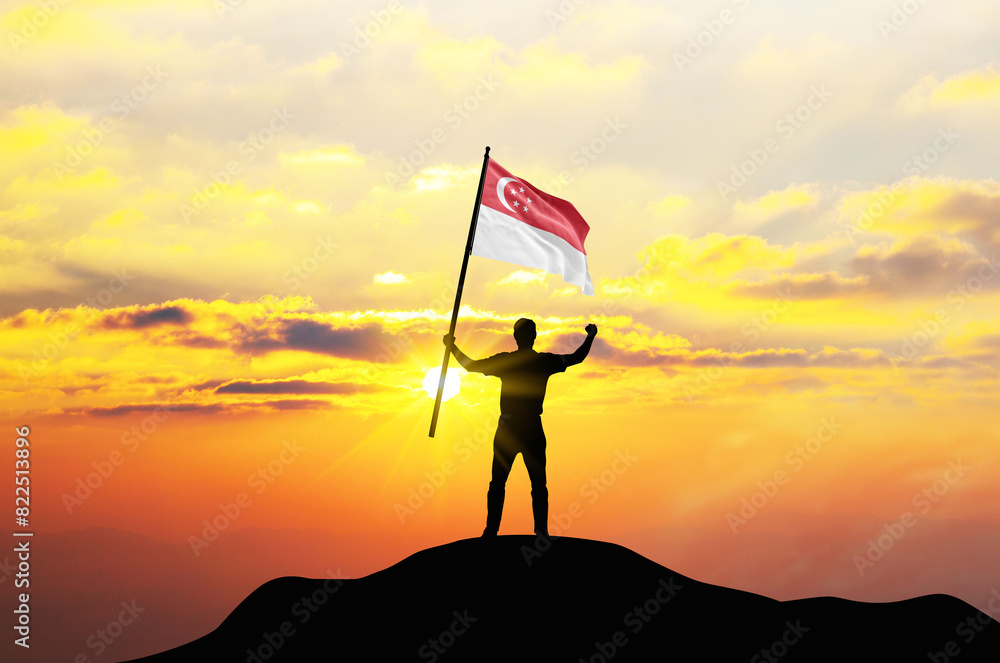 Singapore flag being waved by a man celebrating success at the top of a mountain against sunset or sunrise. Singapore flag for Independence Day.