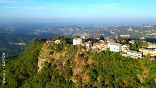 Smooth aerial push-in shot from Smerillo (Fermo) with the manyfold white and beige buildings of the village sitting on a lone mountainous cliff almost suspended among vast visuals of Marche hillscapes photo