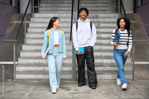 Three young students are walking up a set of stairs, each carrying a backpack