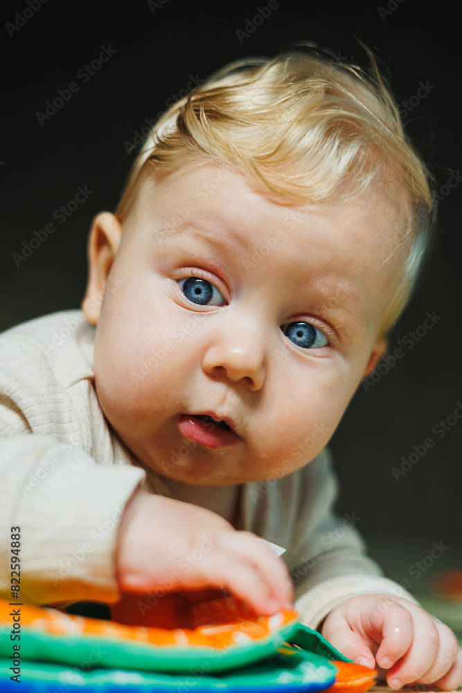 Fototapeta premium A small child in a white bodysuit is learning to crawl on a clean, heated floor. Home photo of a cute blue-eyed baby.