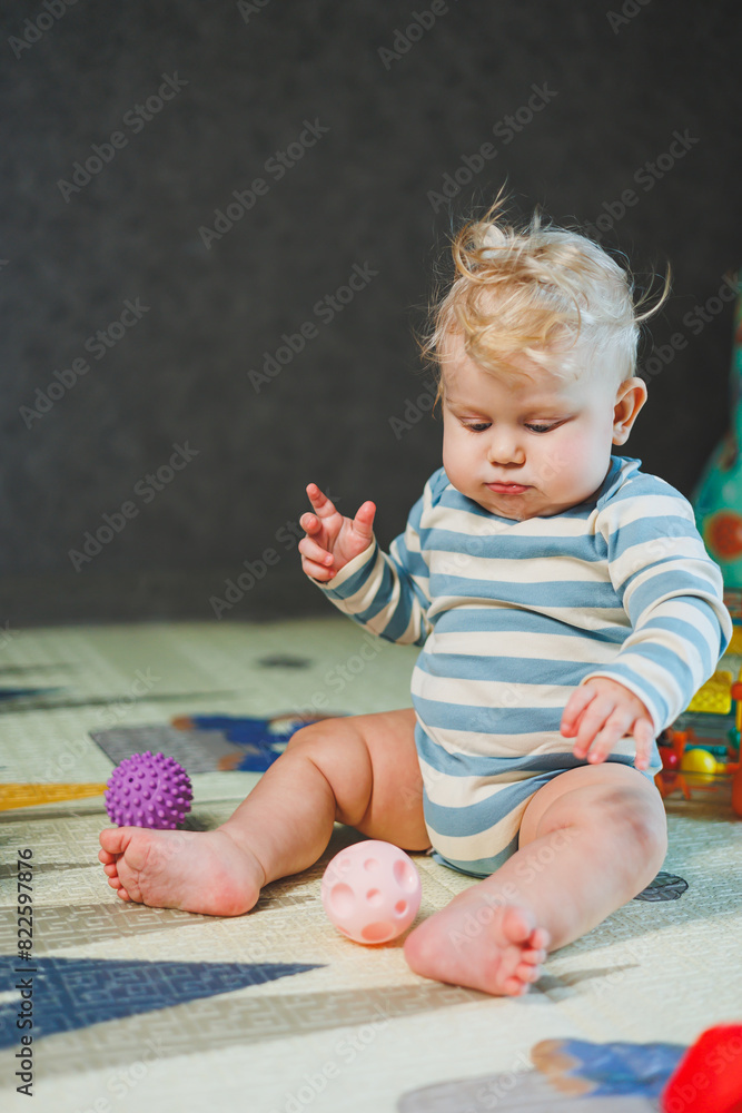 Fototapeta premium A small child in a white bodysuit is learning to crawl on a clean, heated floor. Home photo of a cute blue-eyed baby.