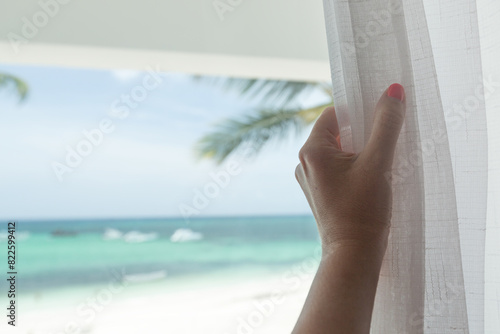 Woman opening curtains and looking on sea view from balcony