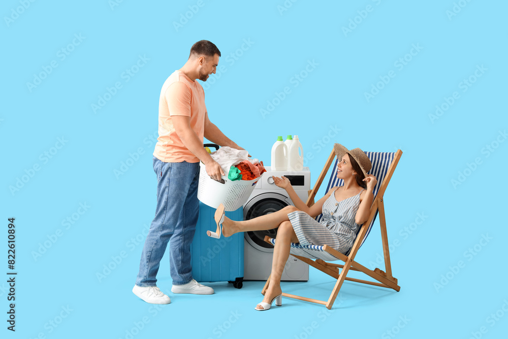 Young woman on vacation and her husband doing laundry on blue background