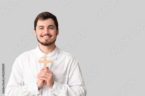 Smiling young man with cross on grey background