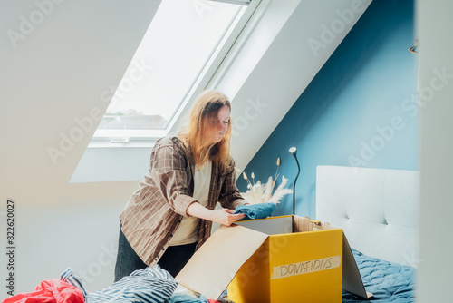 Woman selecting clothes from her wardrobe for recycling, donating to a Charity shop. Decluttering, Sorting clothes, Cleaning Up. Reuse, second hand concept. Conscious consumer, sustainable lifestyle. photo