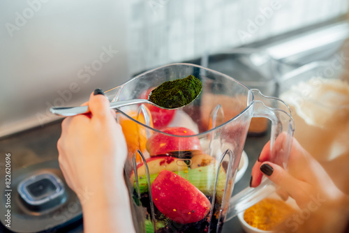 Close up woman adding spirulina or chlorella powder during making smoothie on the kitchen. Superfood supplement. Healthy detox vegan diet. Healthy dieting eating, weight loss program. Selective focus photo