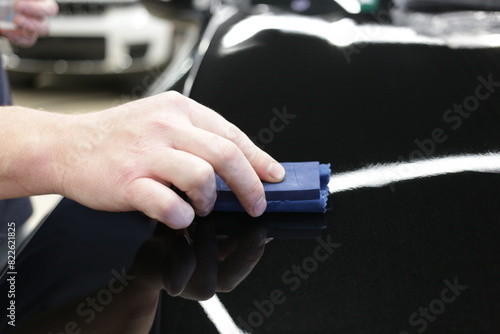 Car service worker applying nano coating on a car detail close-up. Closeup of hand coating black car bonnet paint. Automotive ceramics. 
