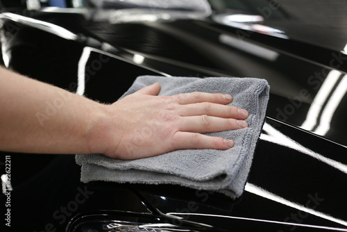 Service worker polishing car with microfiber cloth. Detailing a car - a man holds a soft microfiber in his hand and polishes the body close-up. 