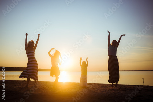 Silhouettes of children and mothers jumping and having fun on the beach in sunset light. Family weekend vibe. Good mood pastime among the generations. Beautiful natural landscape. Childhood happiness