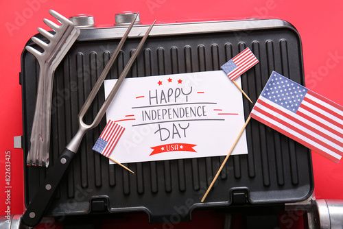 Greeting card with text HAPPY INDEPENDENCE DAY, electric grill and barbecue utensils on red background, closeup