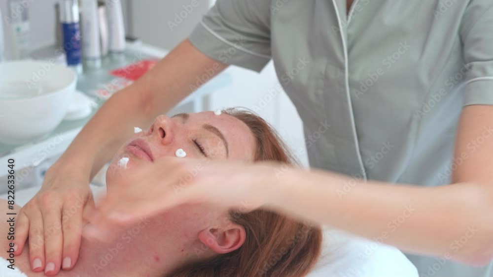 Female dermatologist applying cream on face of beautiful woman lying on bed. Young lady having skincare procedure in beauty salon. Female dermatologist applying cream on face of beautiful woman lying on bed. Young lady having skincare procedure in beauty salon.
