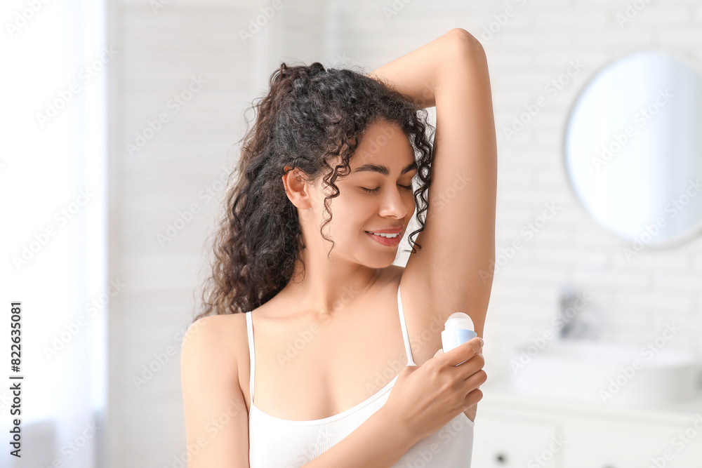 Beautiful young African-American woman applying deodorant in bathroom Beautiful young African-American woman applying deodorant in bathroom