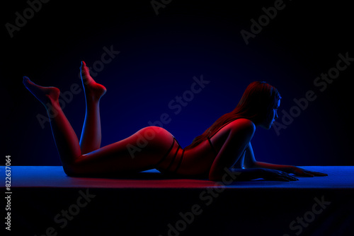 Beautiful young brunette woman lying in sexy lingerie in colored light in studio on a dark background