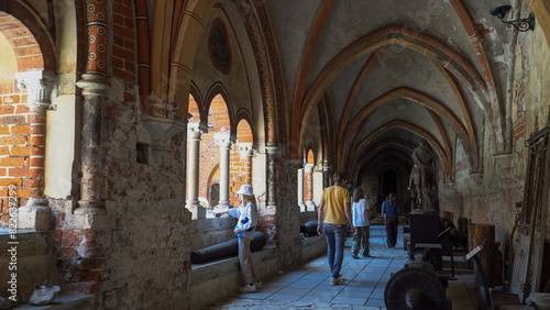 People visit Riga Dome, the Cathedral of Saint Mary, and explore the corridor within a building's courtyard, where historical objects from ancient times are displayed.